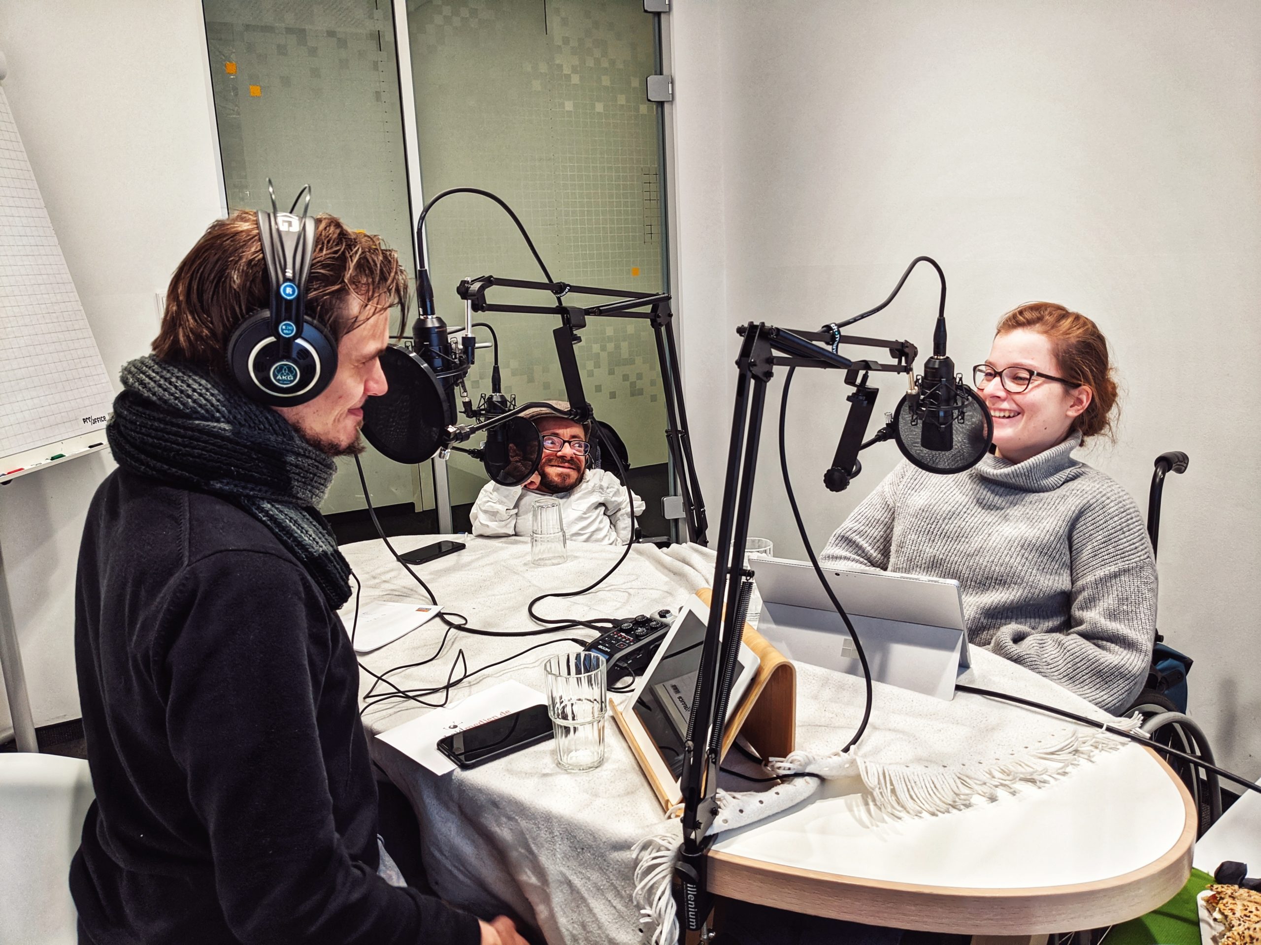 Bild der Aufnahme vom Podcast die Neue Norm, auf dem Bild befinden sich die drei Protagonist:innen an einem Tisch, die Stimmung ist fröhlich.