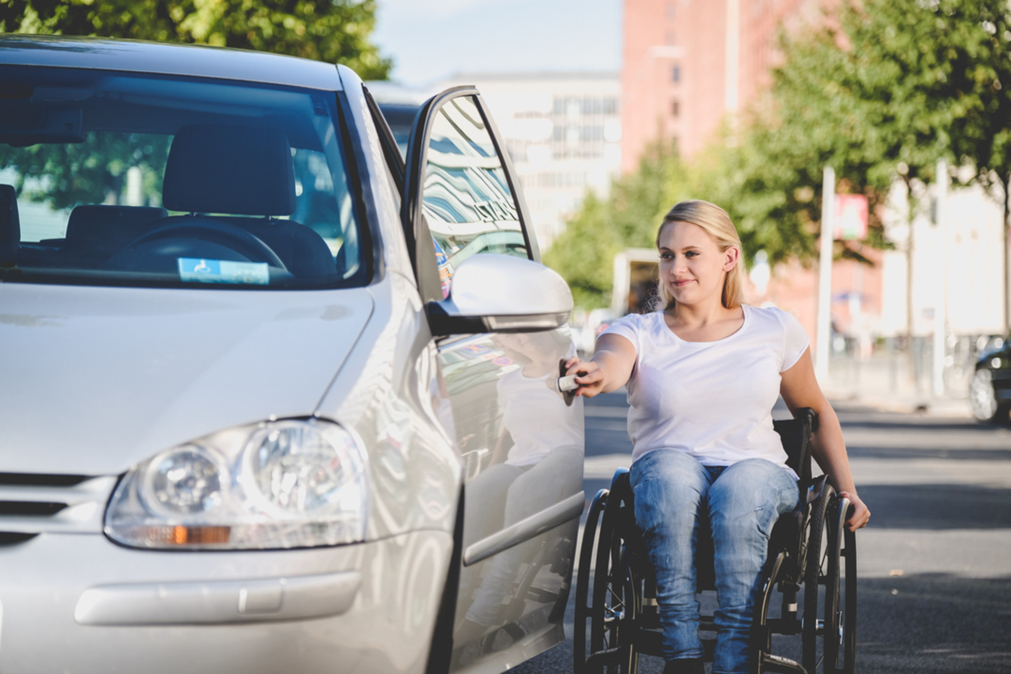Eine Frau, die einen Rollstuhl nutzt, öffnet die Fahrertür eines Autos.